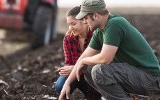 Two farmers kneeling in a field inspecting the soil.