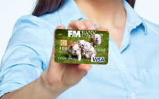A close up on someone's hand holding an F&M debit card. The debit card has puppies on it.